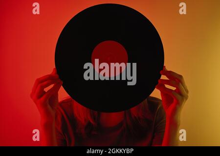 Frau hielt Retro-Vinyl-Disc in den Händen und bedeckte ihr Gesicht, getöntes Foto. Vintage-Stil 80er und 90er Jahre Stockfoto