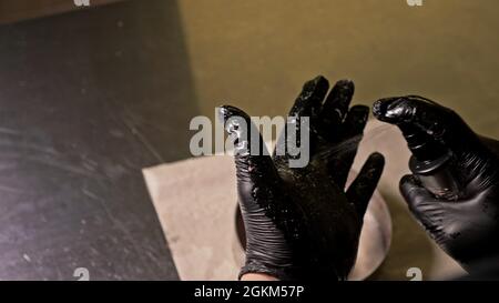 Kochen macht Fleisch Medaillons für Burger. Koch in schwarz Handschuhe macht Schnitzel essen. Die koteletts sind in Stahl Ring in eine noch Medaillon eingeebnet. Stockfoto