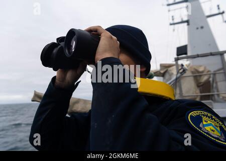 Ein Brückenwachassistent schaut während einer Flag Histing Übung (FLAGEX) durch das Fernglas. Am 23. Mai 2021 führte die Air Defense Frigate (FDA) Forbin im Rahmen der Übung „Formidable Shield 21“ eine FLAGEX-Übung durch, eine Übung zur Kommunikation mit drei anderen Schiffen (amerikanisch, englisch und italienisch). Die Air Defense Frigate (FDA) Forbin nimmt an der kombinierten Luft- und Raketenabwehrübung „Formidable Shield 2021“ vor der Küste des Vereinigten Königreichs Teil. Stockfoto