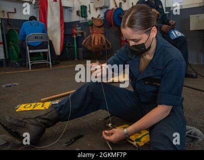 210526-N-ZE328-1071 ATLANTISCHER OZEAN (26. Mai 2021) Seaman Kayla Rafaele aus New Rochelle, New York, verbindet einen Wimpel mit einer Telefon- und Entfernungslinie in der Hangarbucht des Flugzeugträgers USS Harry S. Truman (CVN 75) der Nimitz-Klasse während der Probefahrt, nachdem eine erweiterte Verfügbarkeit der Fluggesellschaft erreicht wurde. Zu den Probefahrten gehört ein umfassender Test der Systeme und Technologien des Schiffes, um sicherzustellen, dass das Schiff bereit ist, den Betrieb wieder aufzunehmen. Stockfoto