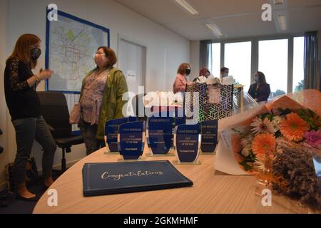 Auszeichnungen, ein Blumenstrauß und Dankesurkunden sitzen auf dem Tisch im Konferenzraum des Army Community Service in der US Army Garrison Benelux - Brüssel; die Ehrengäste und ihre Gäste sprechen vor Beginn der Zeremonie im Hintergrund. Während einer Zeremonie im Mai 27, die virtuell stattfand, erhielten Mitglieder der US Army Garrison Benelux-Gemeinschaft Anerkennung für ihre ehrenamtlichen Aktivitäten für die Jahre 2019 und 2020. Rentner, aktive Dienstmitglieder, Familien, Teams und Zivilisten auf dem Brüsseler Luftwaffenstützpunkt Chievres und DER SHAPE widmeten sich ihrer Zeit der Verbesserung der Lebensqualität ihrer Freunde und ihrer Freunde Stockfoto