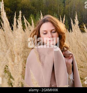 Eine Erwachsene Frau im braunen Mantel geht im Herbstgras in der Natur spazieren Stockfoto