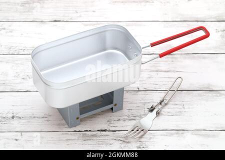 Neues Geschirr aus Stahl für Camping auf einem weiß lackierten Holztisch Stockfoto