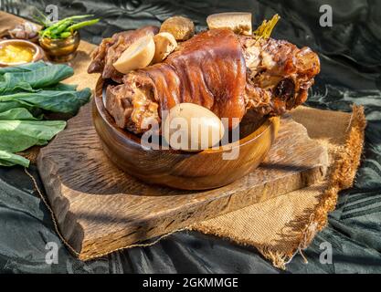 Chinesisches traditionelles Gericht geschmortes Schweinefleisch Bein mit kochender süßen Soße und gekochtem Ei, Tofu, Grünkohl serviert mit eingelegtem Salat und eingelegtem Chili auf b Stockfoto