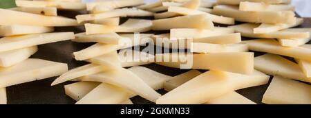 Ausgehärtete Scheiben Manchego-Käse über schwarzem Schiefertablett. Closeup Stockfoto