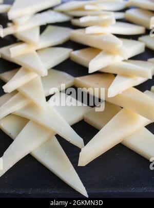 Ausgehärtete Scheiben Manchego-Käse über schwarzem Schiefertablett. Closeup Stockfoto