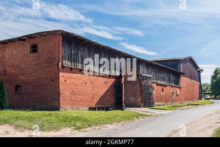 Alte, große, hölzerne und gemauerte Scheune mit offenem Holztor. Sonniger Sommertag im Land. Kopań, Pomorze, Polen Stockfoto