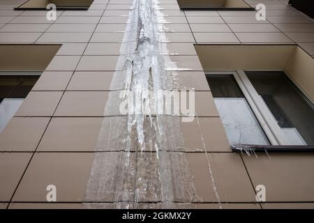 Gefrorene Regenleitung an einem Apartmentgebäude. Eis an der Gebäudewand. Stockfoto