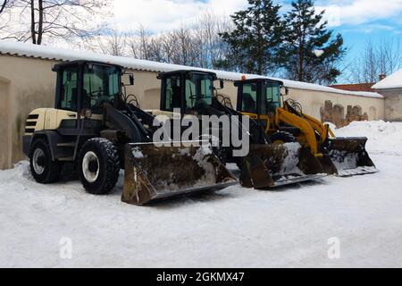 Schwere Erdbeweger, die nebeneinander geparkt wurden, haben Schnee nach dem Schneesturm bewegt. Industriebagger, die Schnee auf den Gehwegen entfernen. Stockfoto