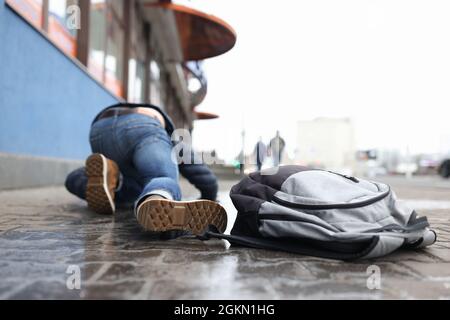 Mann mit Rucksack, der nach dem Sturz in der Nähe auf rutschigem Bürgersteig liegt Stockfoto