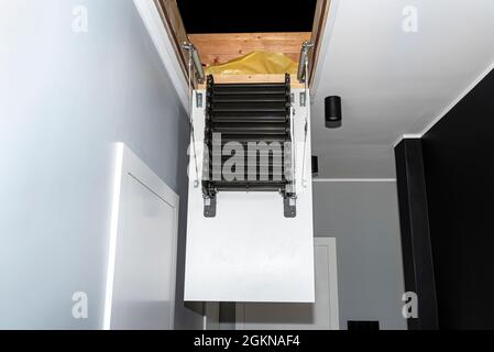 Klappbare Metalltreppe zum Dachboden in der Decke, offene Luke und komplexe Treppe, moderne Optik. Stockfoto