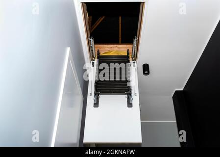 Klappbare Metalltreppe zum Dachboden in der Decke, offene Luke und komplexe Treppe, moderne Optik. Stockfoto