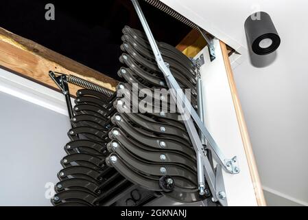 Klappbare Metalltreppe zum Dachboden in der Decke, offene Luke und komplexe Treppe, moderne Optik. Stockfoto