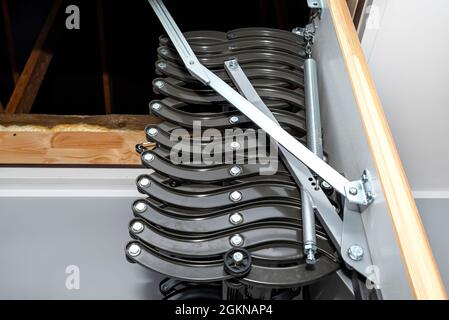 Klappbare Metalltreppe zum Dachboden in der Decke, offene Luke und komplexe Treppe, moderne Optik. Stockfoto