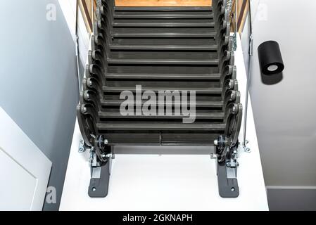 Klappbare Metalltreppe zum Dachboden in der Decke, offene Luke und komplexe Treppe, moderne Optik. Stockfoto