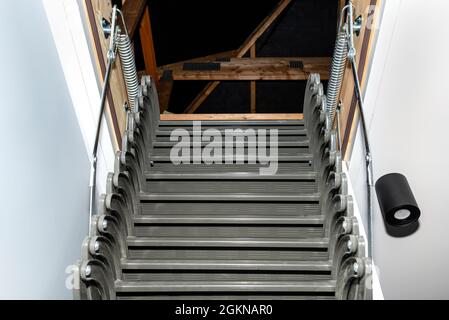 Klappbare Metalltreppe zum Dachboden in der Decke, offene Luke und komplexe Treppe, moderne Optik. Stockfoto