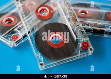 Mehrere transparente, kompakte Audiokassetten mit sichtbarem Klebeband und roten inneren Rollen, die zufällig auf einem blauen Hintergrund platziert werden. Selektive Fokusmethode Stockfoto