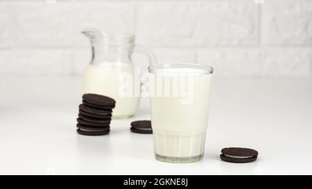 Volle Tasse Milch, neben einem Stapel runder Schokoladenkekse auf einem weißen Tisch Stockfoto