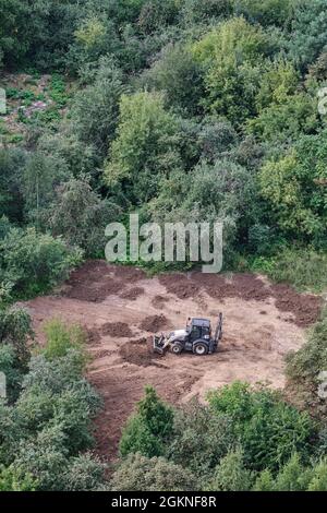 Der Bagger bereitet den Boden auf dem Feld im Wald unter den Bäumen für die Landschaftsgestaltung und Landwirtschaft, Draufsicht - Moskau, Russland, 24. August 2021 Stockfoto