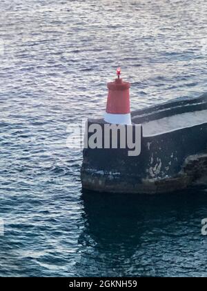 Rot-weißer Leuchtturm am Mittelmeer (Binnenmeer) mit wolkenlosem Himmel und Sonnenuntergang Stockfoto