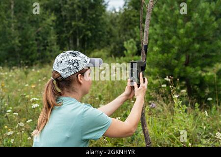 Junge Frau Wissenschaftler Biologe Zoologe stellt Kamera Falle für die Beobachtung von wilden Tieren im Sommer Taiga Wald zu sammeln wissenschaftliche Daten Umwelt Stockfoto