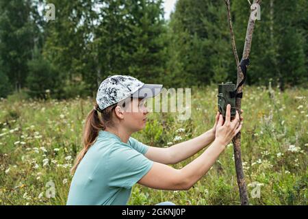 Junge Frau Wissenschaftler Biologe Zoologe stellt Kamera Falle für die Beobachtung von wilden Tieren im Sommer Taiga Wald zu sammeln wissenschaftliche Daten Umwelt Stockfoto