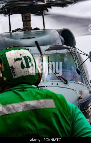 210607-N-JW440-2404 PHILIPPINISCHES MEER (7. Juni 2021) Navy Aircrew Survival Equipmentman 2. Klasse Michael Velezrodriguez, aus Lajas, Puerto Rico, sendet Signale an Piloten in einem MH-60R Seahawk, von den „Saberhawks“ des Helicopter Maritime Strike Squadron (HSM) 77, auf dem Flugdeck der Ticonderoga-Klasse Shiloh CG (Kreuzer 67). Shiloh ist dem Kommandanten der Task Force 70/Carrier Strike Group 5 angeschlossen, der laufende Operationen zur Unterstützung eines freien und offenen Indo-Pazifik-Raums durchführt. Stockfoto