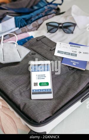 Koffer für Geschäftsreisende mit einem kovidierten Reisepass auf dem Handy Stockfoto