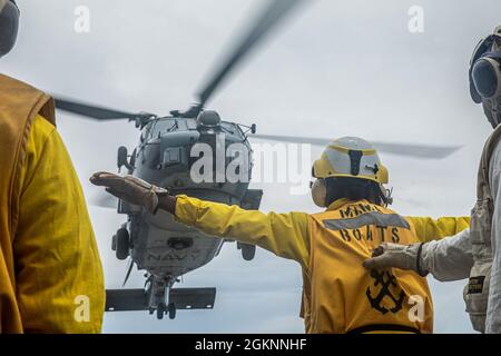 210607-N-XU073-1324 SÜDCHINESISCHES MEER (7. Juni 2021) – Seeleute an Bord der USS Curtis Wilbur (DDG 54) der Arleigh Burke-Klasse signalisieren einen MH-60R Sea Hawk, der der Royal Australian Navy Anzac-Klasse HMAS Ballarat (FFH 155) auf dem Flugdeck zugewiesen wurde. Curtis Wilbur ist Kommandant der Task Force 71/Destroyer Squadron (DESRON) 15, der größten vorwärtseingesetzten DESRON der Marine und der wichtigsten Surface Force der 7. US-Flotte. Stockfoto