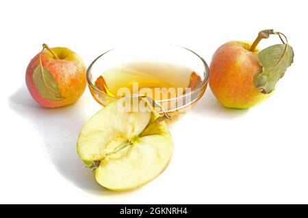 Zwei Äpfel mit Blättern, eine Hälfte Apfel mit grünem Blatt und eine Schüssel mit Apfelessig. Stockfoto