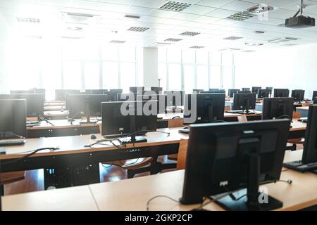 Leeres Großraumbüro mit mehreren Arbeitsplätzen mit Desktop-Computern in einem modernen Büro, einer Hochschule oder einem Callcenter mit Blick auf helle Fenster und Stockfoto