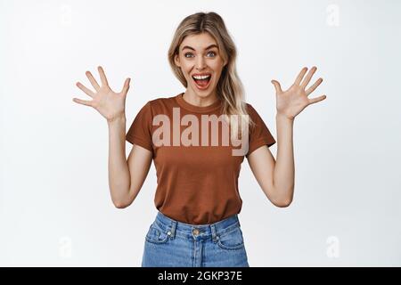 Aufgeregt lächelnde Frau, die leere Hände schüttelt und überrascht aussieht und vor weißem Hintergrund staunt steht Stockfoto