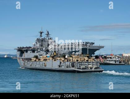 WHITE BEACH, Japan (Jun. 10, 2021) Ein Landungsschiff-Dienstprogramm verlässt das kleine Bootsbecken auf Commander, Fleet Activities Okinawa White Beach Naval Facility, Okinawa, Japan 10. Juni 2021. Das amphibische Angriffsschiff USS America (LHA 6) der amerikanischen Klasse liegt an der Pier-Seite im Hintergrund. Stockfoto