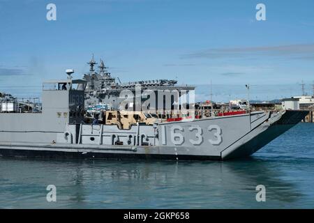 WHITE BEACH, Japan (Jun. 10, 2021) Ein Landungsschiff-Dienstprogramm verlässt das kleine Bootsbecken auf Commander, Fleet Activities Okinawa White Beach Naval Facility, Okinawa, Japan 10. Juni 2021. Das amphibische Angriffsschiff USS America (LHA 6) der amerikanischen Klasse liegt an der Pier-Seite im Hintergrund. Stockfoto