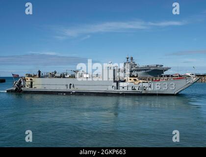 WHITE BEACH, Japan (Jun. 10, 2021) Ein Landungsschiff-Dienstprogramm verlässt das kleine Bootsbecken auf Commander, Fleet Activities Okinawa White Beach Naval Facility, Okinawa, Japan 10. Juni 2021. Das amphibische Angriffsschiff USS America (LHA 6) der amerikanischen Klasse liegt an der Pier-Seite im Hintergrund. Stockfoto