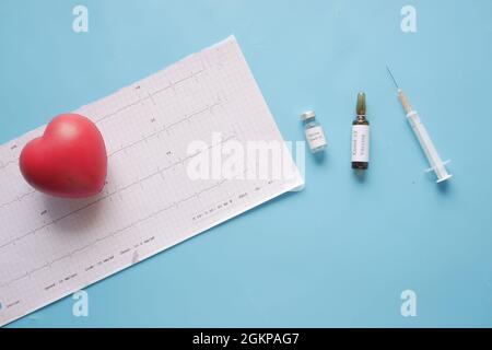 Coronavirus-Impfstoff, Spritze und EKG-Diagramm auf blauem Hintergrund Stockfoto