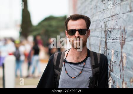 Junger Mann mit Bart und Sonnenbrille, der draußen in der Nähe der Wand steht. Stockfoto