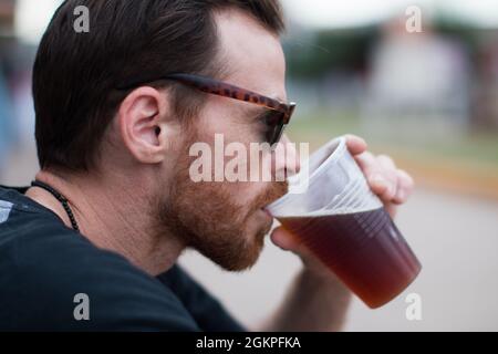 Nahaufnahme des Mannes, der ein Bier aus einem Plastikbecher trinkt. Stockfoto