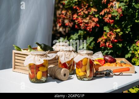 Konservierung Gartengemüse, Konservierung von Tomaten, Paprika, Zucchini-Gemüse. Gemüsekonserven in Gläsern auf dem Tisch im Garten Stockfoto