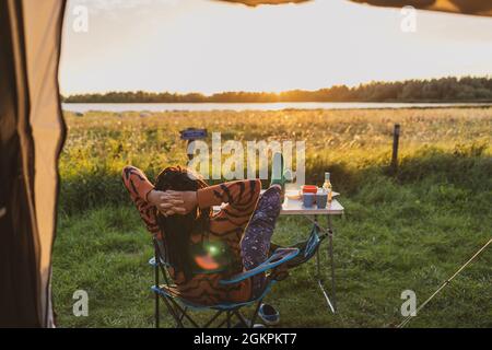 Frau, die sich während des Sonnenuntergangs vor dem Zelt entspannt Stockfoto
