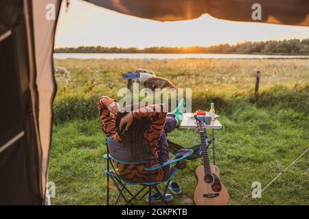 Frau, die sich während des Sonnenuntergangs vor dem Zelt entspannt Stockfoto