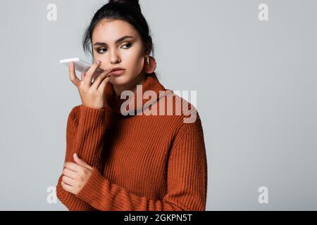 Junge Frau im Strickpullover, die Sprachnachrichten auf dem Smartphone auf Grau aufgezeichnet hat Stockfoto