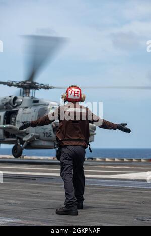 210615-N-ML137-1095 SOUTH CHINA SEA (15. Juni 2021) Aviation Electronics Technician 3rd Class Adrian Buie, aus Garner, North Carolina, beauftragt mit den Saberhawks of Helicopter Maritime Strike Squadron (HSM) 77, Signalisiert einem MH-60R Seahawk, vom Flugdeck des einzigen vorwärts eingesetzten Flugzeugträgers der US-Marine USS Ronald Reagan (CVN 76) abzuheben. Ronald Reagan, das Flaggschiff der Carrier Strike Group 5, stellt eine kampfbereite Truppe bereit, die die Vereinigten Staaten sowie die kollektiven maritimen Interessen ihrer Verbündeten und Partner in der Indo-Pazifik-Region schützt und verteidigt. Stockfoto