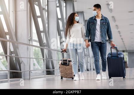 Nahöstliches Paar Mit Gesichtsschutzmasken Beim Gehen Mit Koffern Am Flughafen Stockfoto