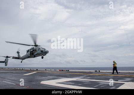 PHILIPPINE SEA (15. Juni 2021) Aviation Boatswain's Mate (Handling) 3rd Class Edward Stewart aus Suffolk, VA., der dem nach vorne eingesetzten amphibischen Sturmschiff USS America (LHA 6) zugeordnet ist, signalisiert einen MH-60S Sea Hawk Hubschrauber vom Helicopter Sea Combat Squadron (HSC) 25 zum Start auf dem Flugdeck des Schiffes. Amerika, das führende Schiff der America Amphibious Ready Group, arbeitet zusammen mit der 31. Marine Expeditionary Unit im Einsatzgebiet der 7. US-Flotte, um die Interoperabilität mit Verbündeten und Partnern zu verbessern und als einsatzbereite Einsatztruppe zur Verteidigung von Frieden und Stabilität im in-Raum zu dienen Stockfoto
