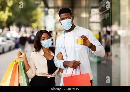 Porträt eines glücklichen schwarzen Paares in Masken mit Kreditkarte Stockfoto