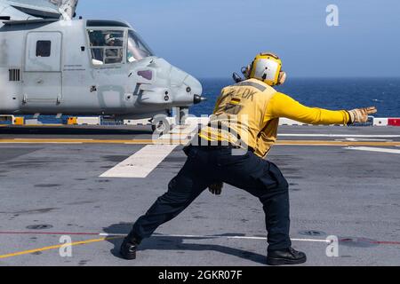 PHILIPPINISCHE SEE (16. Juni 2021) Aviation Boatswain's Mate (Handling) 3rd Class Edward Stewart aus Suffolk, VA., der dem forward-eingesetzten amphibischen Sturmschiff USS America (LHA 6) zugewiesen wurde, signalisiert einen MV-22B Osprey der 31st Marine Expeditionary Unit (MEU) zum Start. Amerika, das führende Schiff der America Amphibious Ready Group, ist zusammen mit der 31. MEU im Einsatzgebiet der 7. US-Flotte tätig, um die Interoperabilität mit Verbündeten und Partnern zu verbessern und als einsatzbereite Einsatztruppe zur Verteidigung von Frieden und Stabilität in der Indo-Pazifik-Region zu dienen. Stockfoto