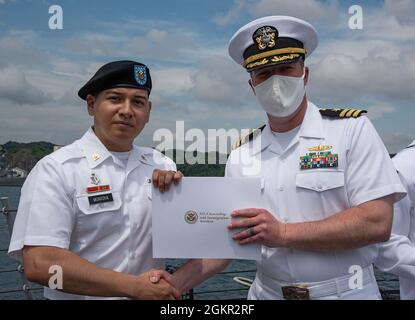 YOKOSUKA, Japan (17. Juni 2021) – SPC der US-Armee. Rigoberto Montoya Arcega, ein gebürtiger Mexikaner, der der medizinischen Abteilung Activity Japan im Camp Zama angeschlossen ist, erhält von Cmdr ein Staatsbürgerschaftszertifikat. Matthew Hays, Executive Officer der USS Milius (DDG 69), stationiert bei Commander, Fleet Activities Yokosuka (CFAY) während einer Einbürgerungszeremonie an Bord von Milius. Seit mehr als 75 Jahren bietet, pflegt und betreibt CFAY Basiseinrichtungen und -Dienste zur Unterstützung der im Vorlauf eingesetzten Seestreitkräfte der US-amerikanischen 7. Flotte, der Pächter-Kommandos und Tausender militärischer und ziviler Mitarbeiter an Stockfoto