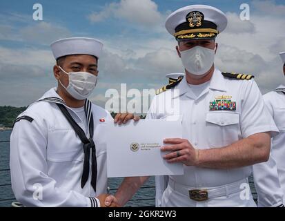 YOKOSUKA, Japan (17. Juni 2021) – der Feuerwehrmann Carl Jefferson Robles Dela Cruz, ein gebürtiger Philippiner, der der USS Milius (DDG 69) angeschlossen ist, erhält von Cmdr ein Staatsbürgerschaftszertifikat. Matthew Hays, Executive Officer der USS Milius (DDG 69), stationiert bei Commander, Fleet Activities Yokosuka (CFAY) während einer Einbürgerungszeremonie an Bord von Milius. Seit mehr als 75 Jahren stellt, pflegt und betreibt CFAY Basiseinrichtungen und -Dienste zur Unterstützung der im Einsatz kommenden Seestreitkräfte der 7. US-Flotte, der Pächter-Kommandos und Tausender militärischer und ziviler Mitarbeiter und ihrer Familien. Stockfoto