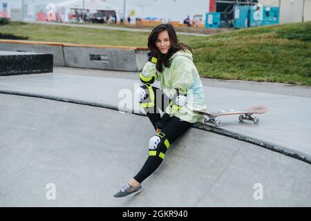 Porträt einer lächelnden, schönen Skaterin, die auf einem Deck ruht. Stockfoto